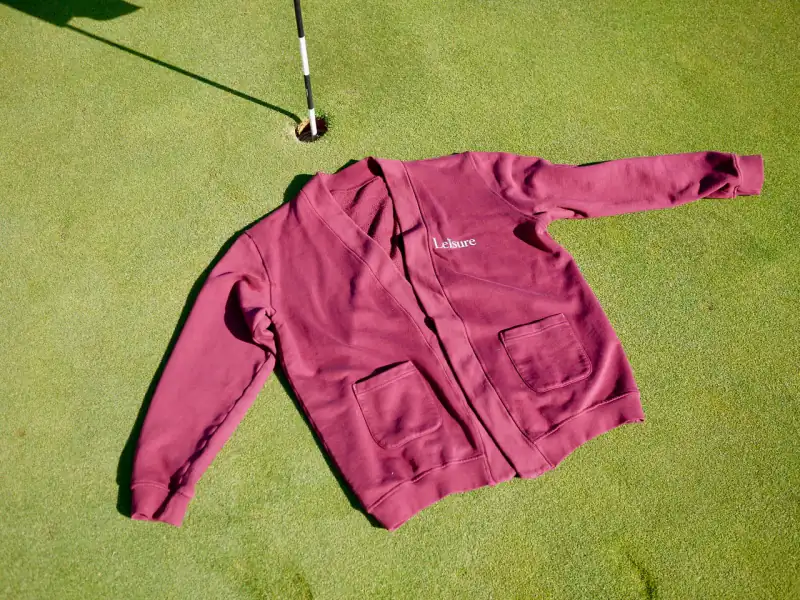 The Chubbs Cardigan in burgundy laid flat on a putting green — Leisure on the chest, two patch pockets