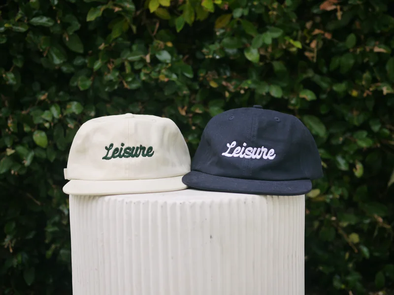 The Players Cap in cream and navy — Leisure script across the front, side by side on a pedestal